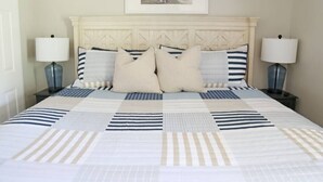 Una cama bien hecha con ropa de cama a rayas, dos lámparas de noche y un cuadro en la pared.