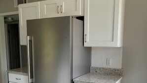 Una cocina con armarios blancos, un refrigerador de acero inoxidable y un bote de basura.