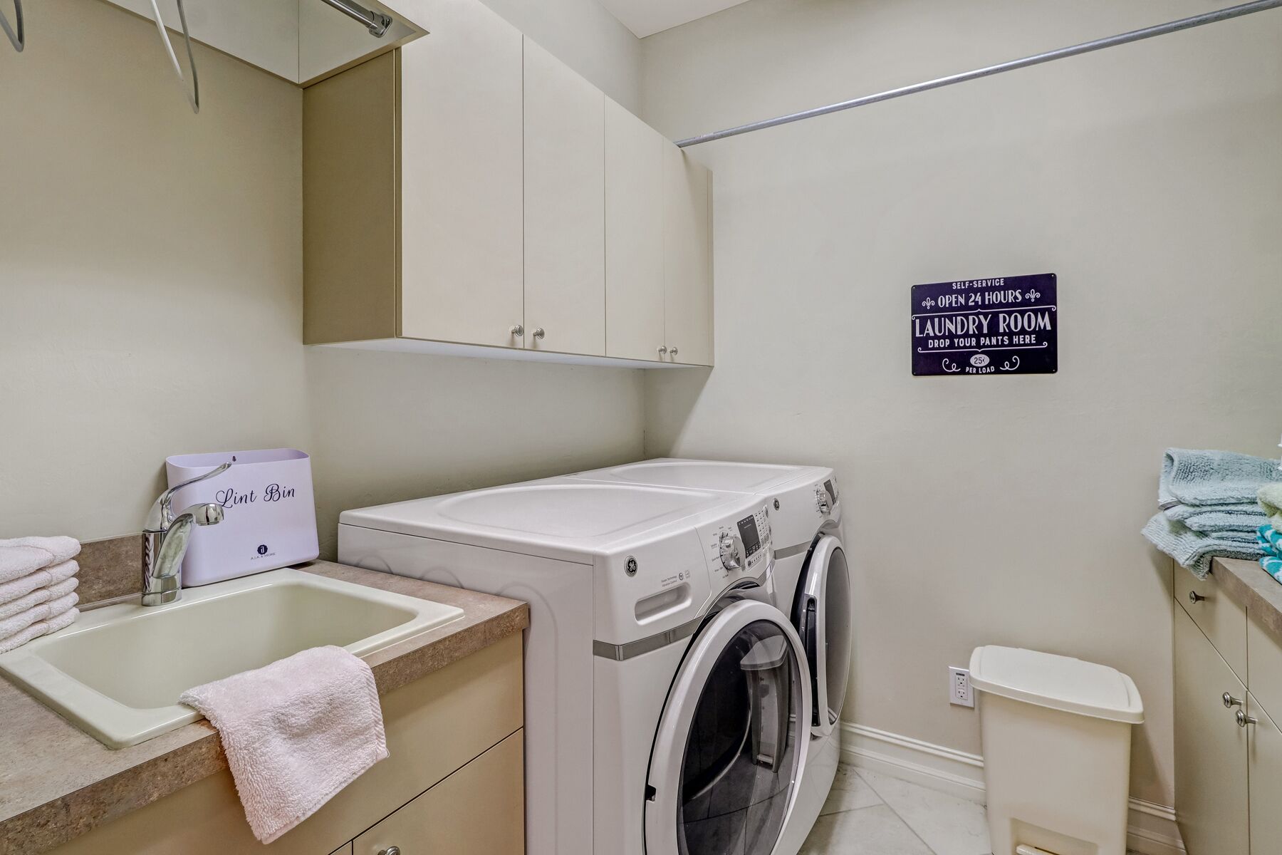 Een wasruimte met een wasmachine, een wastafel en een bord dat aangeeft dat deze 24 uur per dag open is.