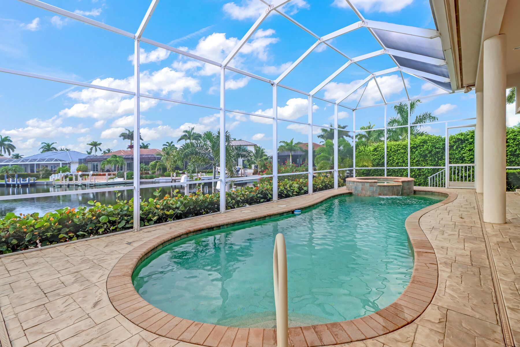 An indoor swimming pool with a clear view of the surrounding landscape, including palm trees and a distant building.