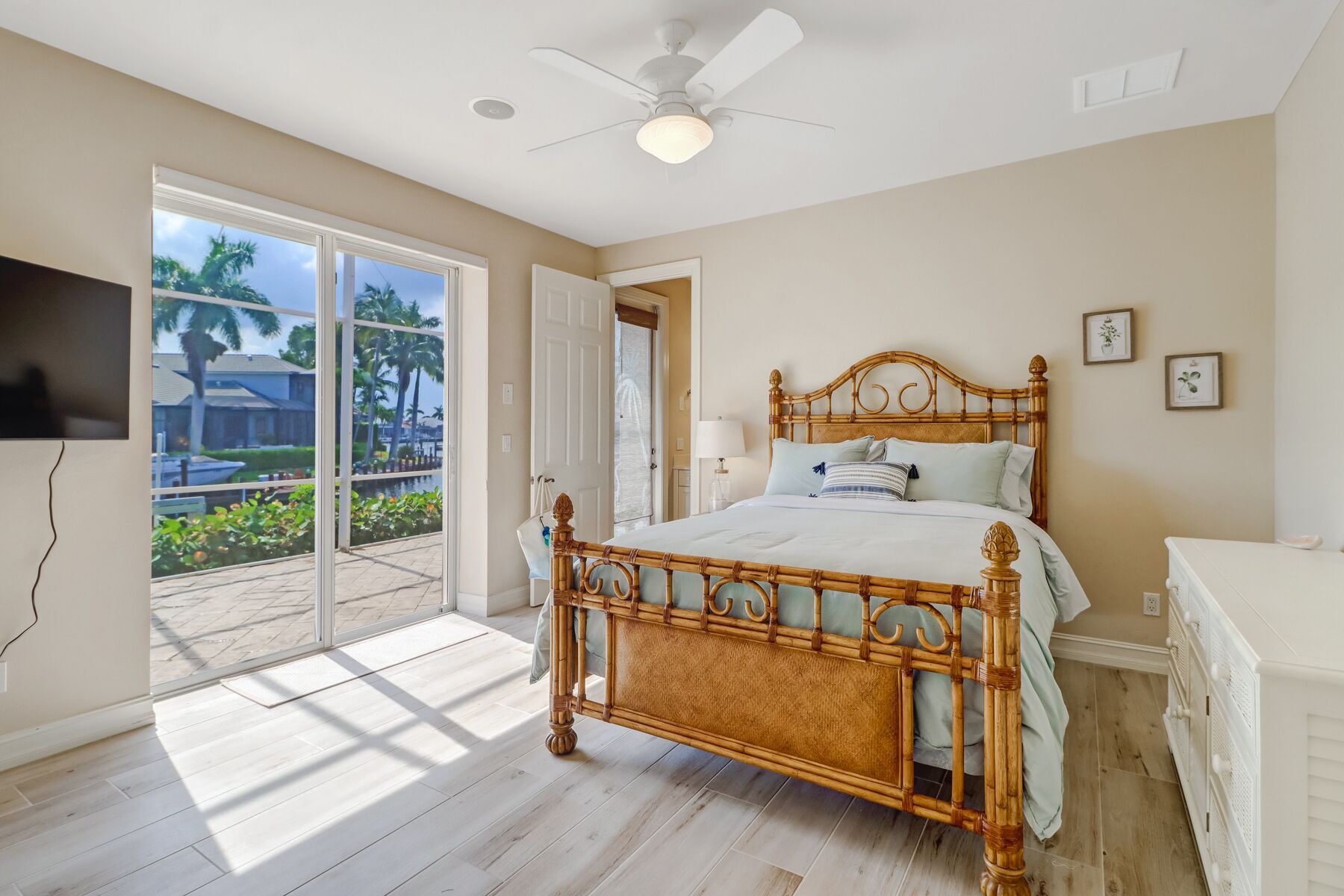 Ein Schlafzimmer mit einem großen Bett, einem Deckenventilator und Blick auf einen Pool und Palmen durch eine Schiebetür.