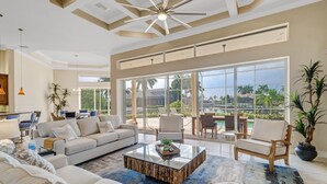 Ein geräumiges Wohnzimmer mit einer großen Couch, einem Couchtisch und Blick auf einen Pool und Palmen.