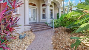 Ein Haus mit einer Veranda, Stufen zum Eingang und einem Garten mit Kies und tropischen Pflanzen.