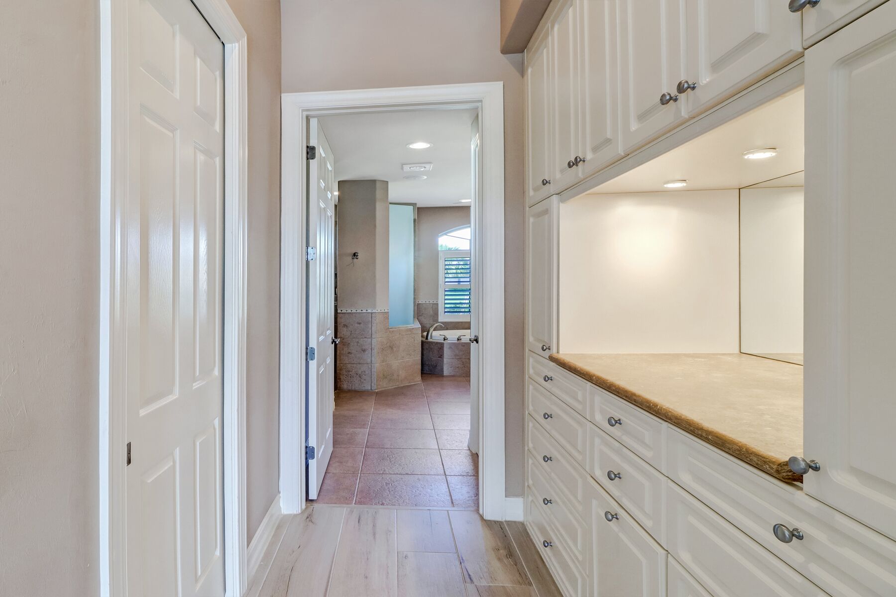 A hallway with white cabinetry and a large mirror.