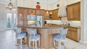 Eine moderne Küche mit Holzschränken, einer zentralen Kochinsel mit Barhocker, Edelstahlgeräten und Pendelleuchten.