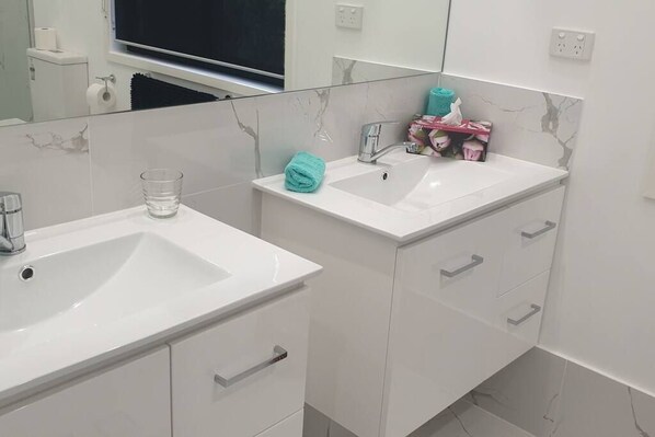 Une salle de bain avec deux lavabos blancs, un miroir et un porte-serviettes.