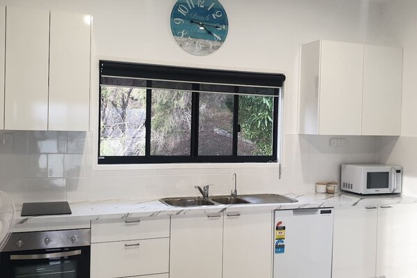 A modern kitchen with white cabinets, a double sink, a microwave, and a clock on the wall. - Sunset Beach House 1770 Level 3 (Seventeen Seventy)