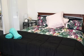 Cama bem arrumada com colcha floral, edredom preto e duas toalhas enroladas.