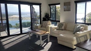 Un salon spacieux avec un canapé blanc, une table basse et une vue sur une étendue d’eau grâce à de grandes fenêtres.