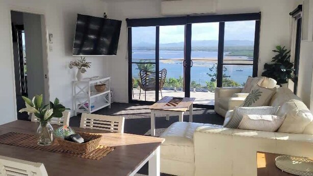 Un salon avec une table en bois, un canapé blanc et un téléviseur fixé au mur.