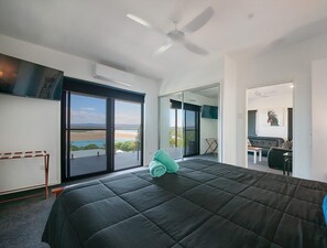A modern hotel room with a large bed, a ceiling fan, a view through a sliding door, and a balcony. - Sunset Beach House 1770 Level 3 (Seventeen Seventy)