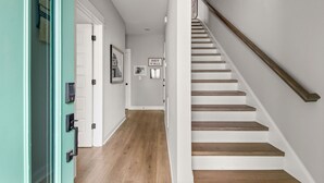 Un pasillo con escalera de madera, una puerta con cerradura electrónica y un letrero que dice "HEY Y'ALL".