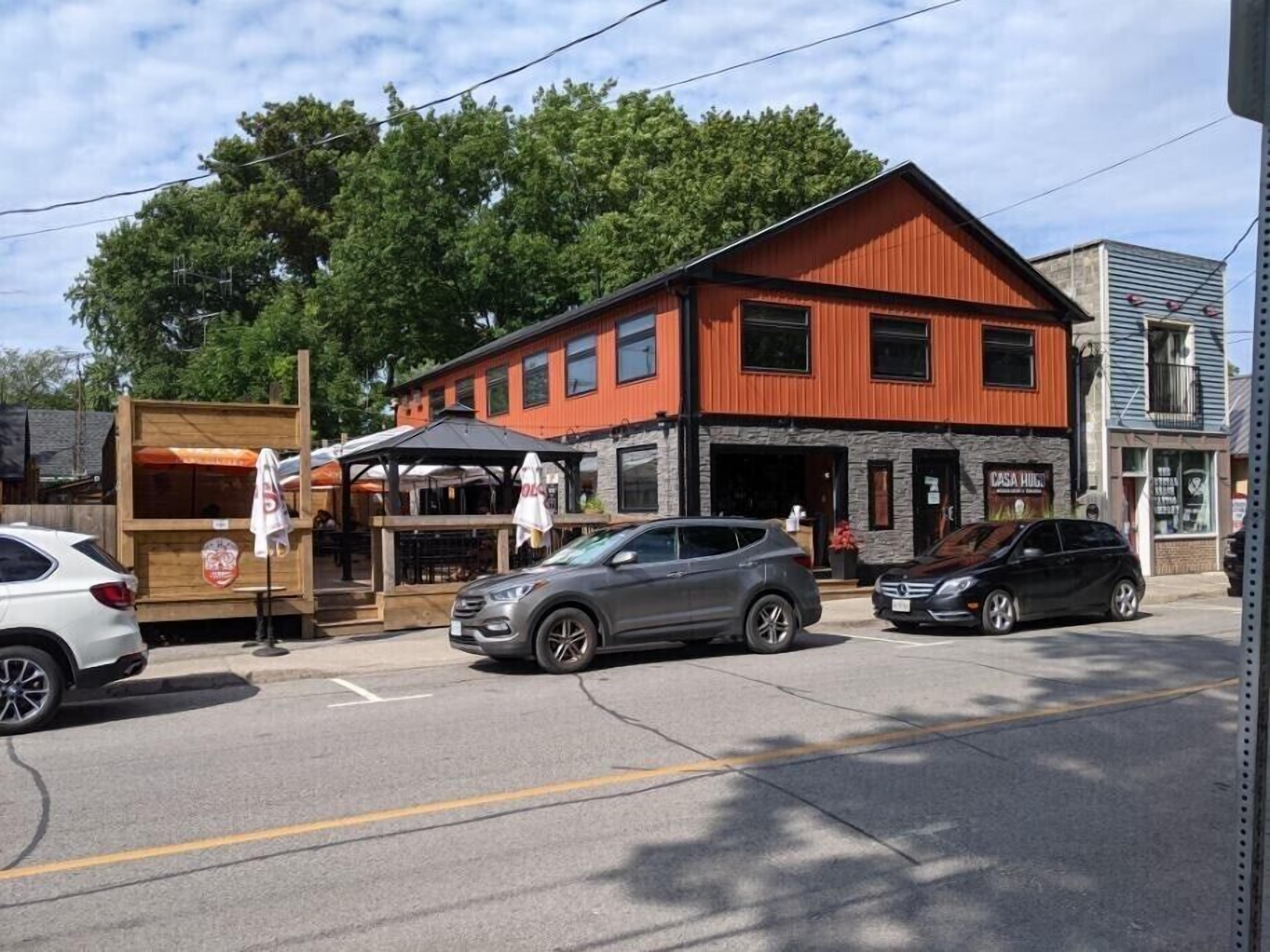 A two-story building with a red facade and a stone base, featuring a restaurant with outdoor seating and a sign that reads "Casa Hugo."