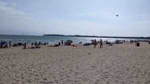 Una playa con gente relajándose y una cometa volando en el cielo.