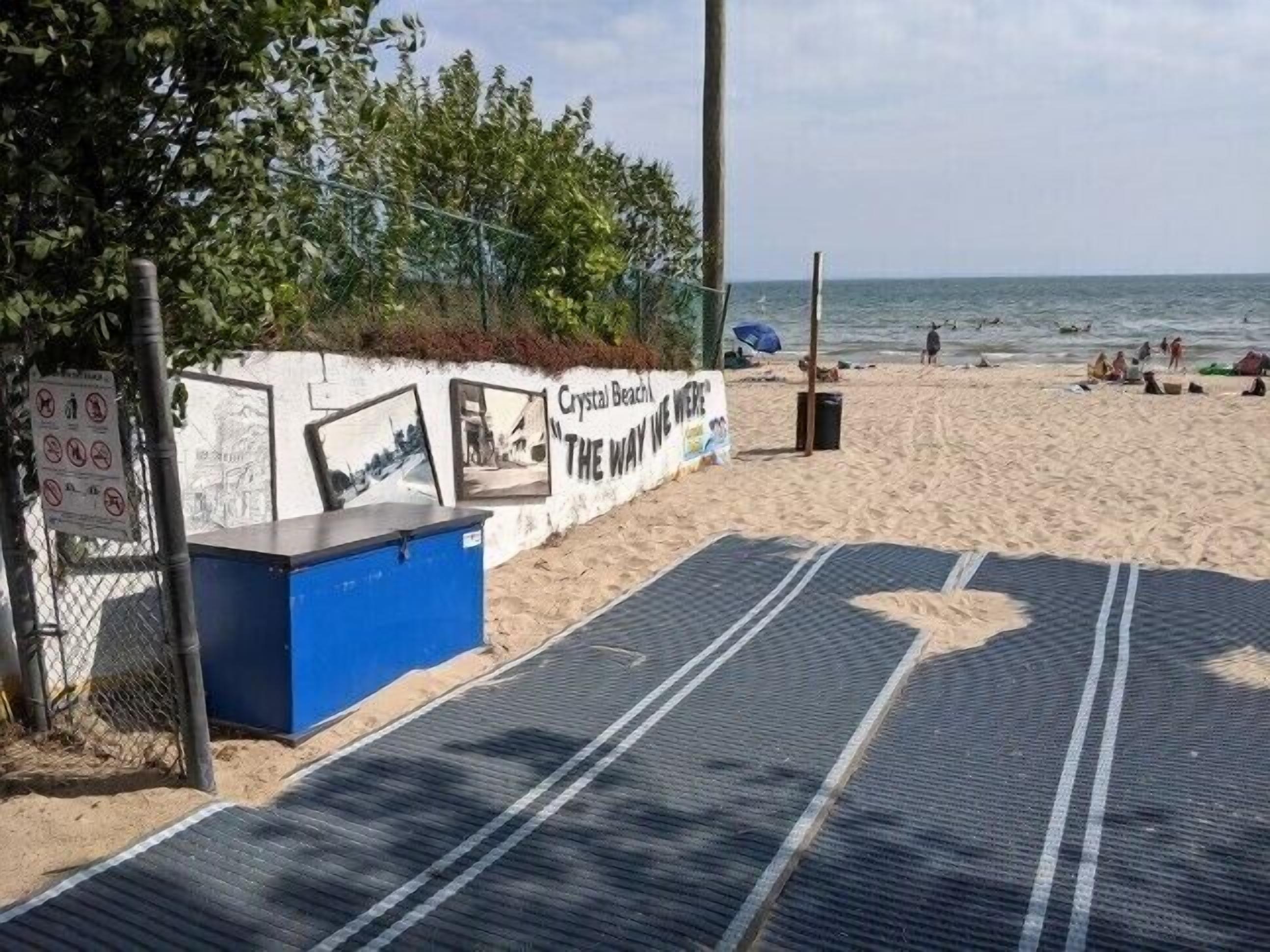 Una playa con un muro que muestra fotografías y un letrero que dice "Crystal Beach THE WAY WE WERE".