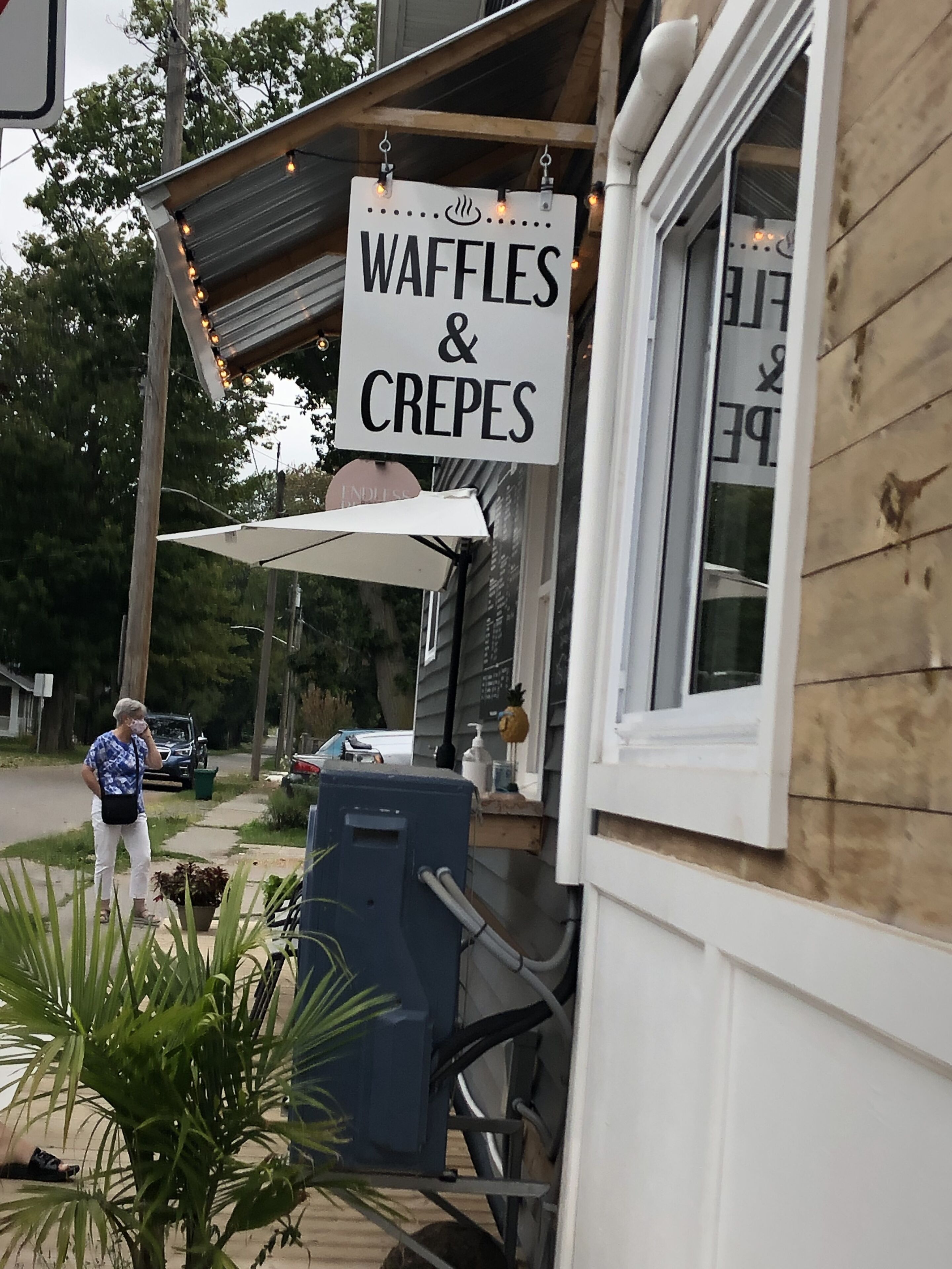 A sign for waffles and crepes hanging outside a building.