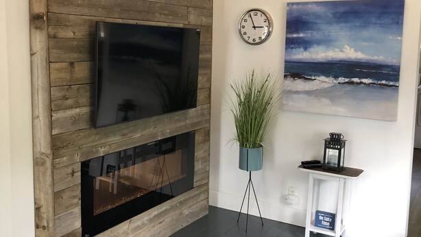 Una sala de estar moderna con un televisor de madera montado en la pared, una chimenea, un reloj y un cuadro del océano.