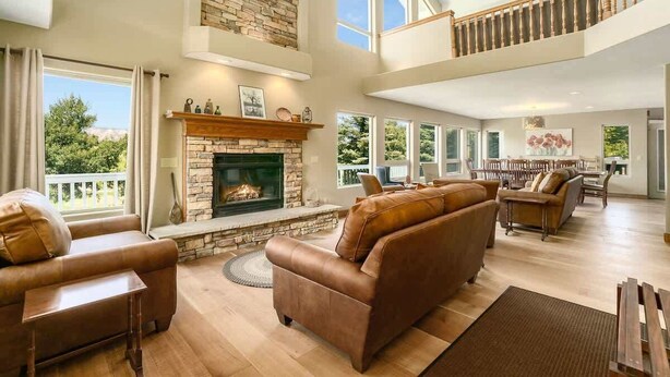 A spacious living room with a stone fireplace, leather sofas, and a high ceiling with large windows.