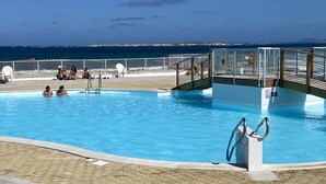 Una piscina con vista al océano, una caseta de salvavidas y una zona cubierta con sillas.