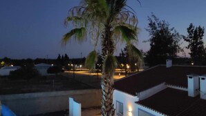A residential area at dusk with a palm tree, streetlights, and houses. - Casa Almeida - Apt. T0 (Vimieiro)