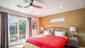 A bedroom with a large bed, a ceiling fan, a nightstand with a lamp, and a view of the outside balcony. - 3bed/3ba home- huge backyard - Mins from Downtown (Houston)