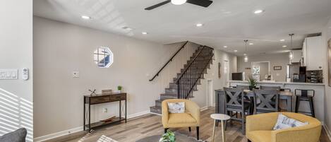 A modern living room with a ceiling fan, a staircase, and a kitchen area.