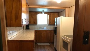 Eine kleine Küche mit Holzausstattung, einem weißen Kühlschrank und einem eingebauten Backofen.