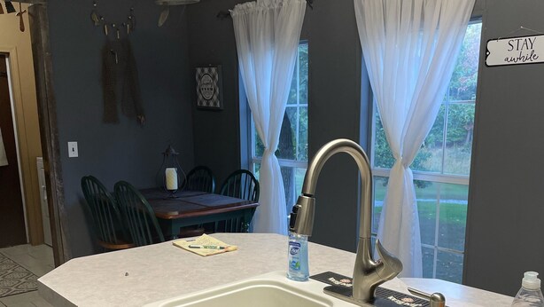 A kitchen with two sinks, a dining area with chairs, and a sign that says "STAY awhile". - Lake Home  (Pontiac)