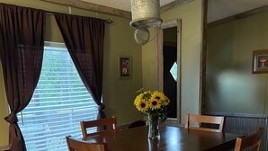A dining room with a wooden table and chairs, a vase with sunflowers, and a window with curtains. - Lake Home  (Pontiac)