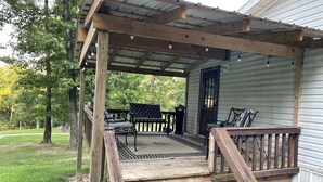 A wooden deck with outdoor furniture, a covered porch, and a view of a forested area. - Lake Home  (Pontiac)