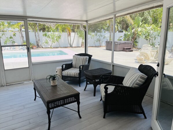 A covered patio with wicker furniture, a small table, and a view of a swimming pool and outdoor seating area. - Splash in Your Own Private Pool and Hot Tub (Fort Pierce)