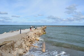 A rocky pier extending into calm waters with people fishing, a distant breakwater, and a clear sky. - Splash in Your Own Private Pool and Hot Tub (Fort Pierce)