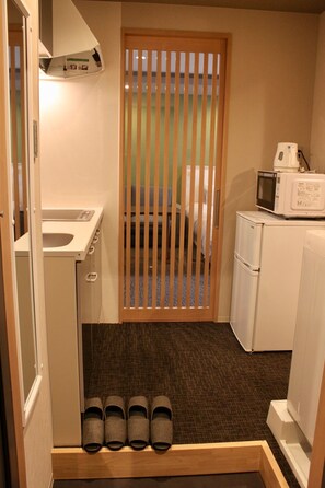 A compact kitchenette with a microwave, a small refrigerator, and a sink. There are shoes neatly arranged at the bottom of the door.