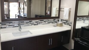 A modern bathroom with a large mirror, a white sink, dark cabinets, and a tiled backsplash.