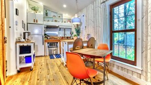 Cocina compacta con comedor, piso de madera y un amplio ventanal con vistas a árboles.