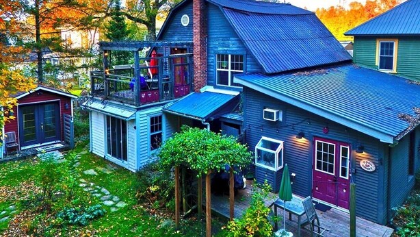 Una casa de varios pisos con un porche, un cobertizo pequeño y un jardín.