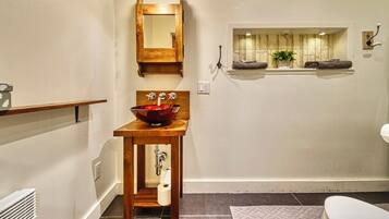 A bathroom with a wooden vanity, a red basin sink, a mirror, a window with a view of trees, and a towel rack.