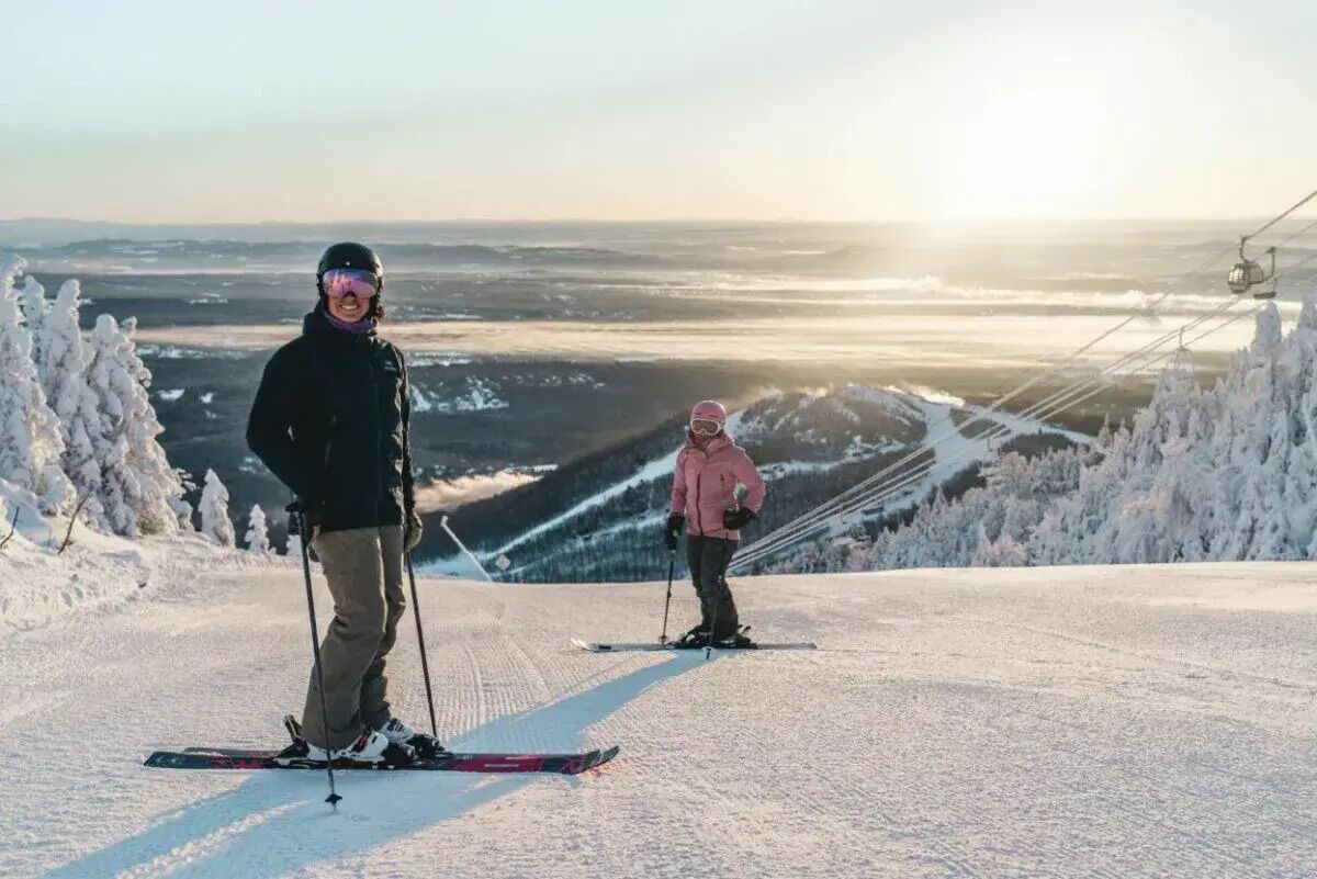 Een skipiste met twee skiërs, één in het zwart en één in het roze, en een kabelbaan op de achtergrond.