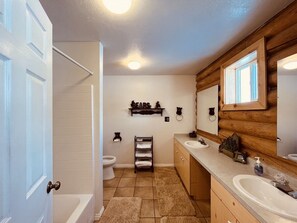 Ein Badezimmer mit einer Badewanne, zwei Waschbecken, einer Toilette und einem Holzwaschtisch.
