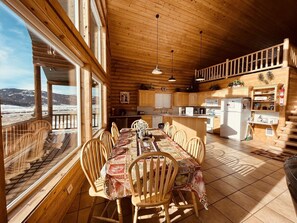 A wooden cabin interior with a dining area, kitchen, and a balcony with a view of the snowy landscape.