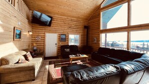 Tunnelmallinen hirsihuvilan sisustus, jossa on olohuone, jossa on sohva, nahkainen lepotuoli, sohvapöytä ja seinälle asennettu televisio.
