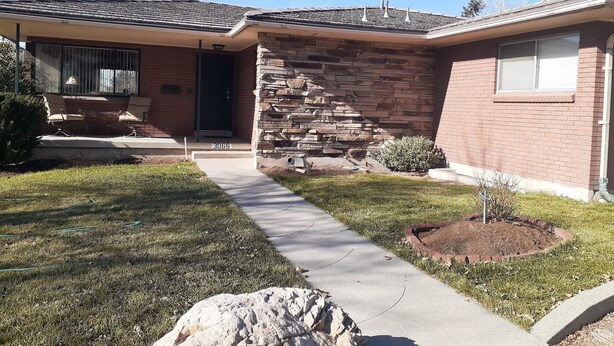 A residential house with a stone facade, a front porch with seating, and a clear sky.