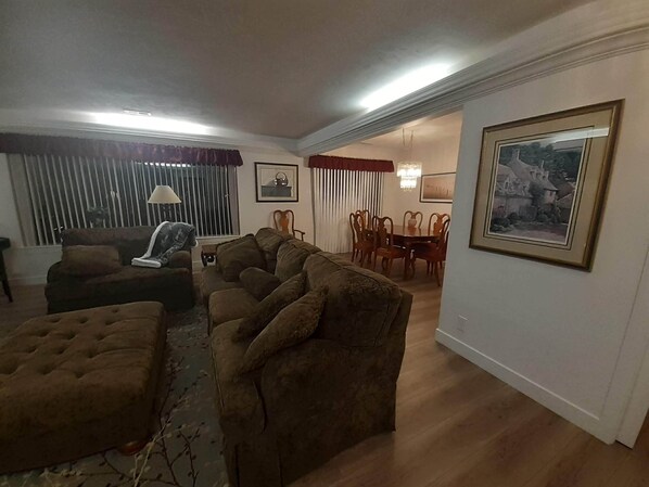 A living room with a sofa, ottoman, dining table, chairs, and a chandelier.