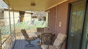 A covered outdoor seating area with a table and chairs, a sliding glass door, and a view of a fenced yard.