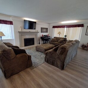 A living room with a fireplace, a flat-screen TV, a piano, and a sofa set.