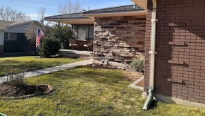 A residential house with a stone facade, a front porch with seating, and a flag.