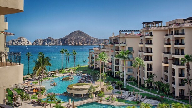 A resort with a central pool, multiple balconies, and a view of the sea and mountains. - New Listing-Newly Renovated-all High End Furnishings! - Medano Beachfront! (Cabo San Lucas)