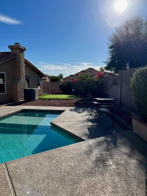A backyard with a swimming pool, a patio table, and chairs. - Large oasis, pool heater, spa, putting green (Avondale)