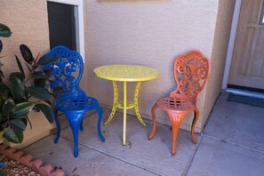 A patio with three chairs and a small round table, positioned against a wall with a door and a potted plant nearby. - Large oasis, pool heater, spa, putting green (Avondale)