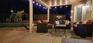 An outdoor patio area with wicker furniture, a pool, and string lights.